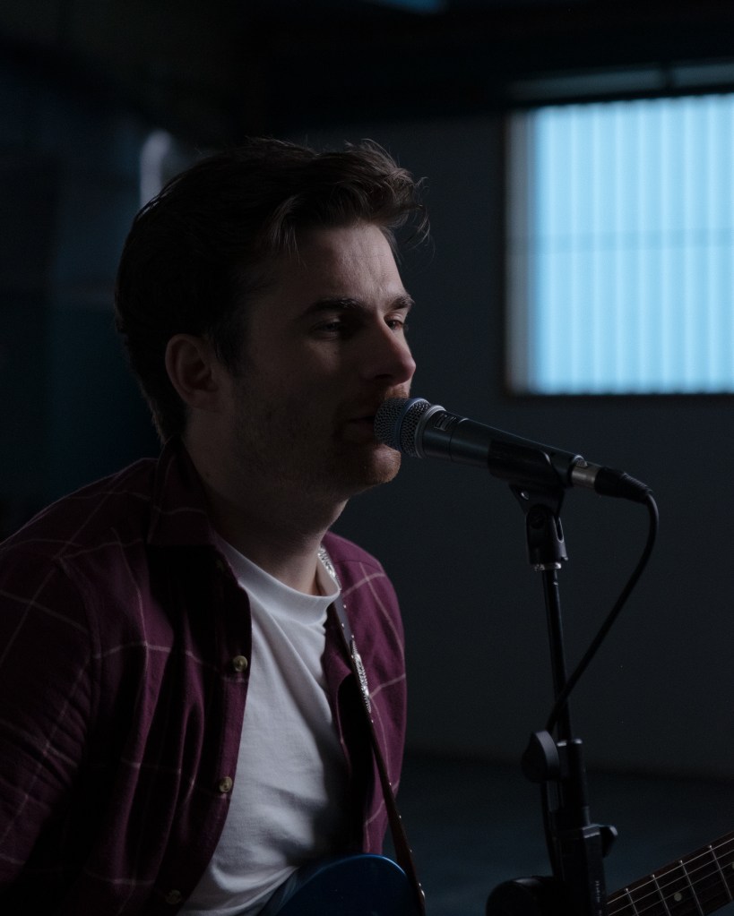 Moody dark shot of a male singer singing into a microphone. Hair and face freshly cut for his music video.